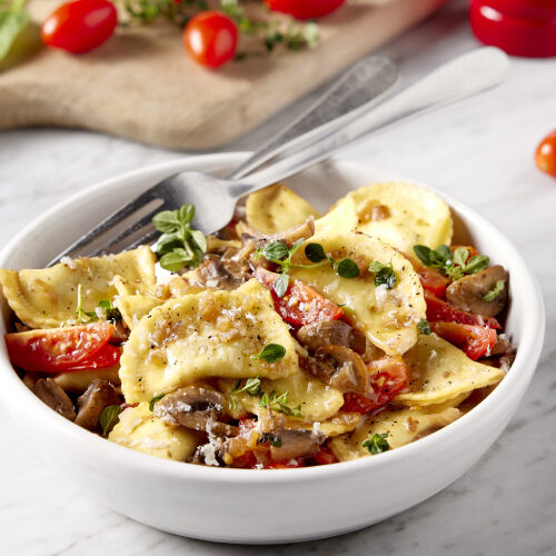 A bowl with pasta recipe and tomatoes spread on table