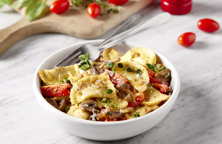 A bowl with pasta recipe and tomatoes spread on table